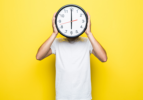 A man holds a clock in front of his face to demonstrate time passing.