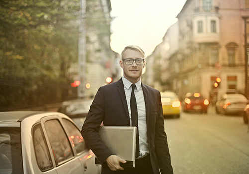 A salesman stands beside his car in the street.