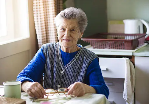An old woman sits in her kitchen.