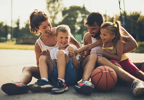 A husband, wife, and their children sit together on a basketball court.