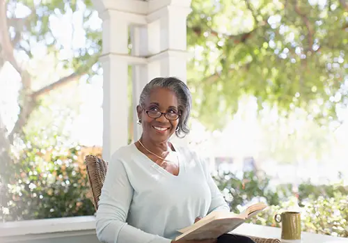 An elderly woman smiles while seated on her porch.