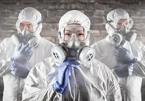 Three people wear hazmat suits indoors.