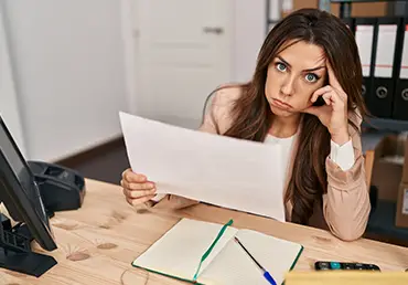 An anxious insurance independent agent sits at her desk and looks directly into the camera.
